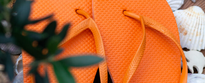 Zwei orangefarbene Flip Flop Schuhe stehen auf Muscheln.