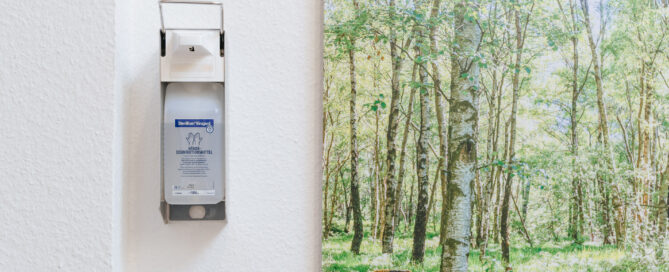 Ein Desinfektionsspender hängt neben einem Bild an der Wand einer Arztpraxis.