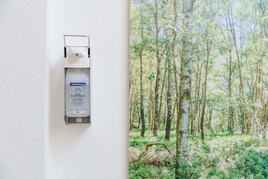 Ein Desinfektionsspender hängt neben einem Bild an der Wand einer Arztpraxis.