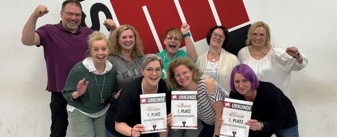 Das Team der Praxis Konzen Monschau posiert bei einem Ausflug vor einem Logo eines Bash-Rooms.