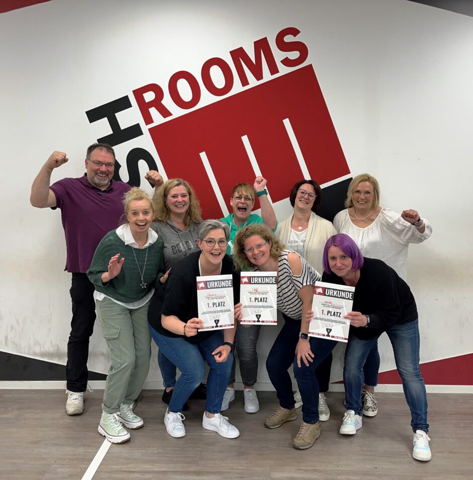 Das Team der Praxis Konzen Monschau posiert bei einem Ausflug vor einem Logo eines Bash-Rooms.