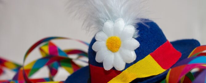 Ein blauer Narrenhut mit Feder und Blume liegt inmitten von Luftschlangen.