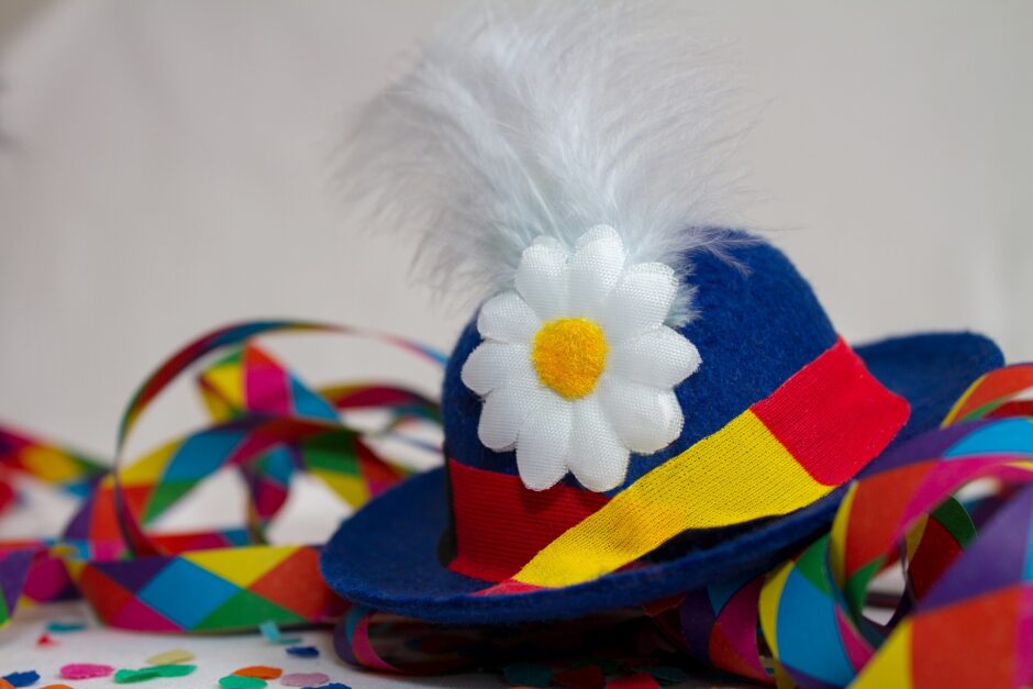 Ein blauer Narrenhut mit Feder und Blume liegt inmitten von Luftschlangen.