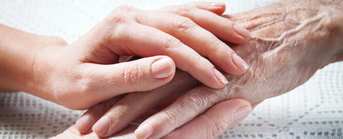 Eine Hand eines jüngeren Menschen hält die Hand eines älteren Menschen.