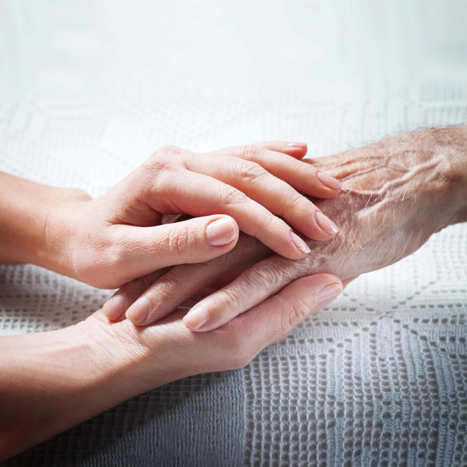 Eine Hand eines jüngeren Menschen hält die Hand eines älteren Menschen.