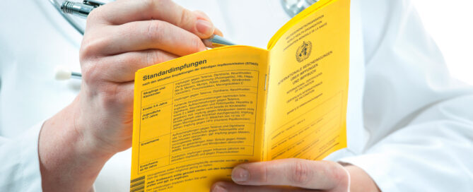 Ein Mensch mit Stetoskop um den Hals trägt etwas in einen Impfpass ein.