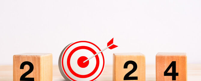 Vier Holzklötze liegen nebeneinander, während einer einer aussieht wie eine Zielscheibe, tragen die anderen Nummern. Zusammen ergeben Sie die Zahl 2024.