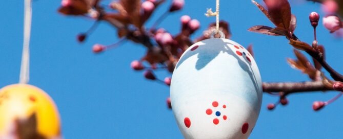 Bunt bemalte Ostereier hängen an einem Baum mit aufgehenden Blüten.