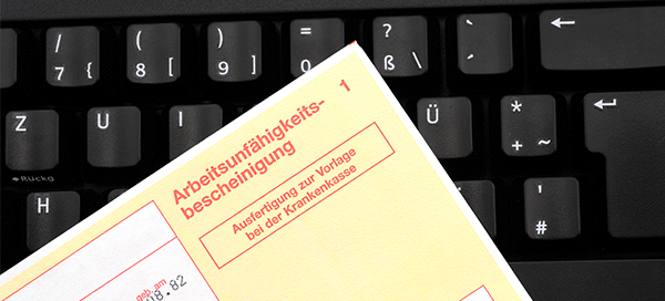 Eine Krankmeldung liegt auf einer Computertastatur.