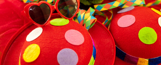 Zwei bunte Hüte, Luftschlangen und eine Herzsonnenbrille liegen vor einer Blume.