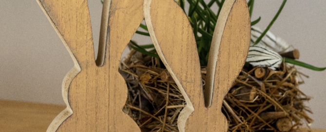 Osterdekoration in Form von zwei Holzhasen steht vor einem Ostergesteck.