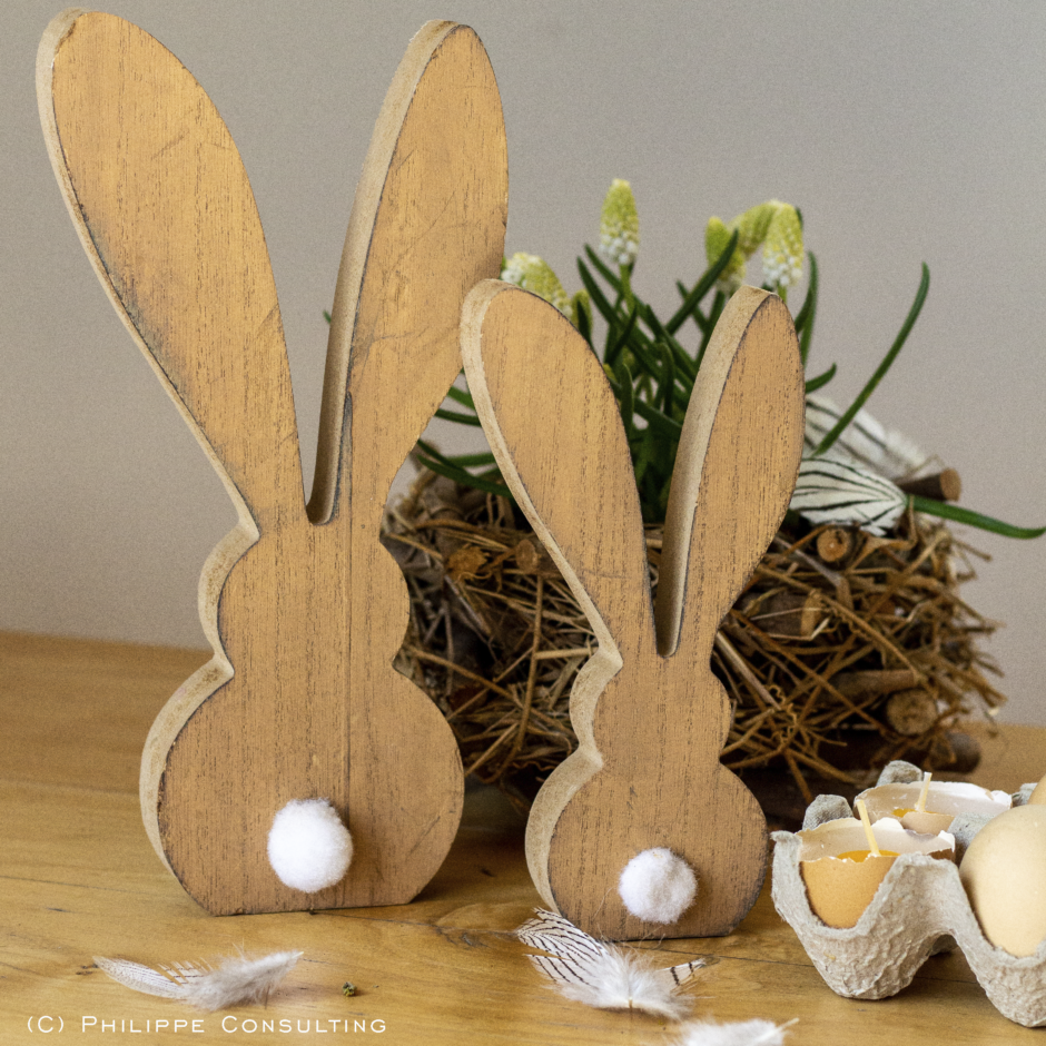 Osterdekoration in Form von zwei Holzhasen steht vor einem Ostergesteck.