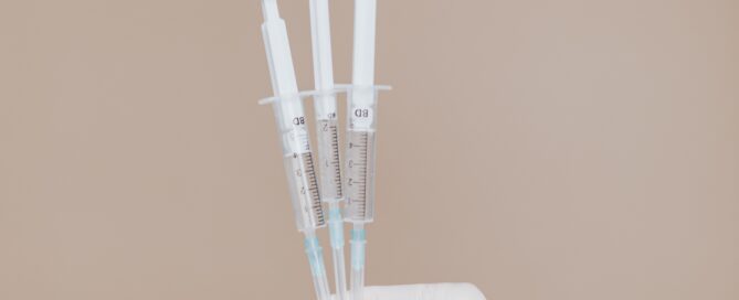 Eine hand mit Gummihandschuh hält drei Spritzen in die Höhe.