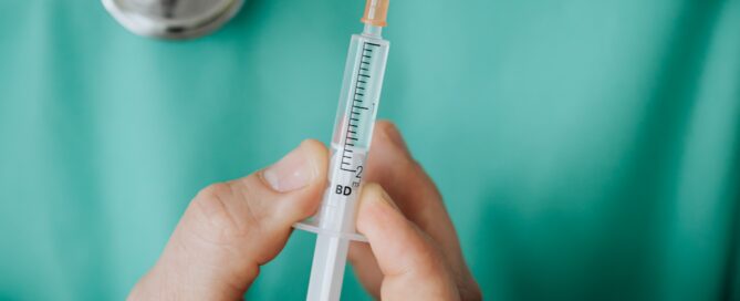 Ein Mensch mit Stetoskop um den hals hält in seinen Händen eine Spritze.