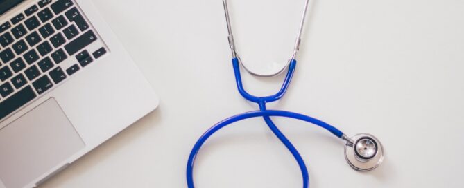 Ein Stetoskop liegt neben einem Laptop.