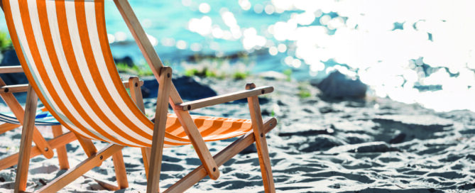 Ein Liegestuhl steht im Sand am Meer in der Sonne.