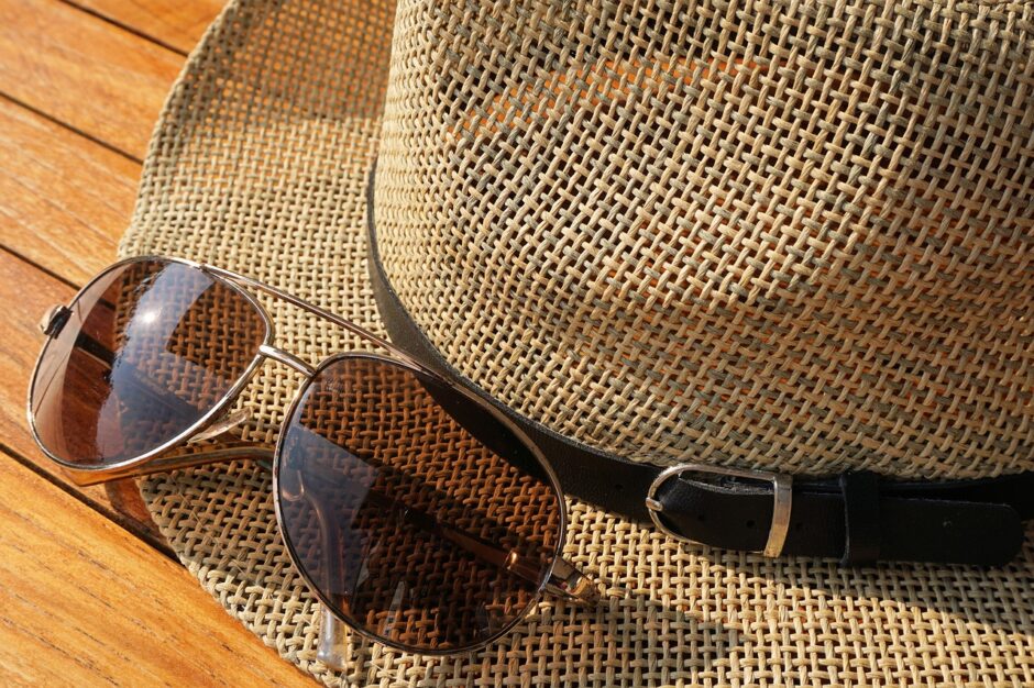 Eine Sonnenbrille liegt neben einem Sonnenhut aus Stroh.