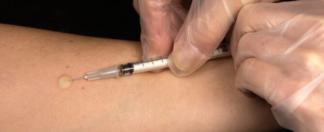 Eine Spritze sticht in einen Arm.