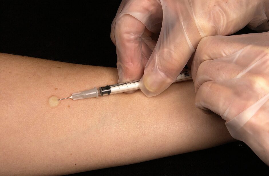 Eine Spritze sticht in einen Arm.